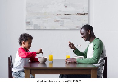 side view of african-american father and son eating breakfast