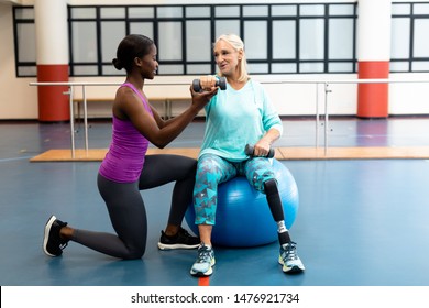 Side view of African-american Female trainer assisting disabled Caucasian senior woman to exercise with dumbbell in sports center. Sports Rehab Centre with physiotherapists and patients working - Powered by Shutterstock