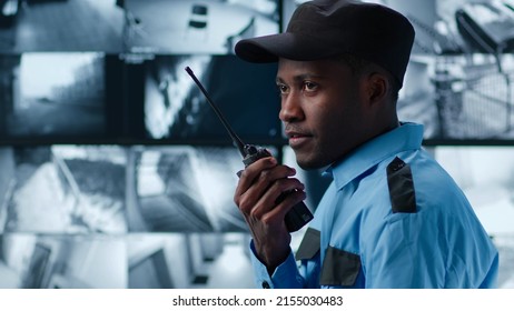 Side View Of African-American Security Guard Talk On Radio In Control Room Monitoring Surveillance Footage