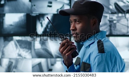 Side view of African-American security guard talk on radio in control room monitoring surveillance footage