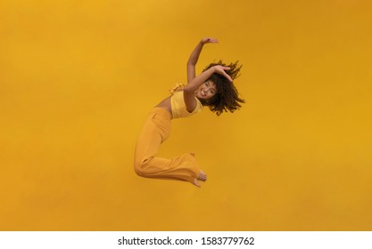 Side View Of Afro Hair Woman In Zero Gravity Or A Fall. Girl Is Flying, Falling Or Floating In The Air. Side View Of Person. Over Yellow Background. Getting Sucked Up. Woman Being Abducted.