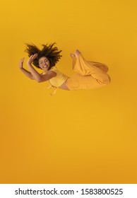 Side View Of Afro Hair Woman In Zero Gravity Or A Fall. Girl Is Flying, Falling Or Floating In The Air. Side View Of Person. Over Yellow Background. Getting Sucked Up. Woman Being Abducted.