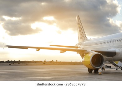 Side view of aircraft wing and engine of large white passenger airplane parked at terminal international airport on runway against dramatic sunset background, getting ready to fly