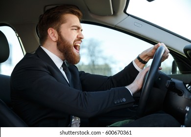 Side view of angry business man in suit driving a car and beeps