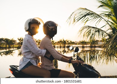 Side View Of Anonymous Couple In Masks And Glasses Driving Motorbike In Helmets And Looking Away While Chilling In Resort