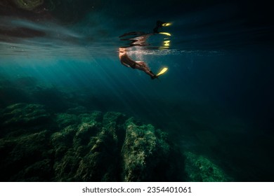 Side view of anonymous male diver in flipper swimming under blue water of deep sea near rough coral reefs