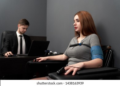 Side View Of Anxious Woman Sitting On Chair While Machine Measuring Pulse During Lie Test. Young Female Answering Questions And Talking Truth While Man Looking At Result. Concept Of Lie Detector.