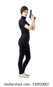 Side view of armed tough woman holding gun looking at camera. Full body length portrait isolated over white studio background.
