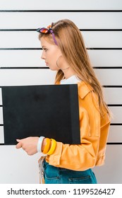 Side View Of Arrested Hipster Girl Posing With Empty Prison Board In Front Of Police Line Up