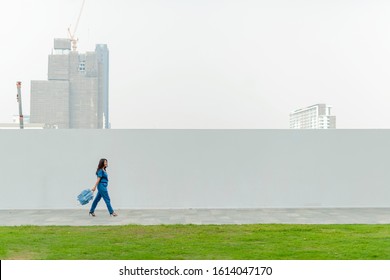 Side View Of Asian Businesswoman Walking On City Street In Front Of Modern Wall And Large Blank Billboard On A Street Wall, Banners To Add Your Own Text.