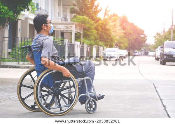 Side view of Asian disabled man wears protective\
mask on wheelchair crossing the street in housing estate, diversity\
people concept