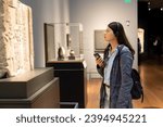 side view of asian Japanese young female on audio tour in an art exhibition. she is admiring a stone carving with concentration