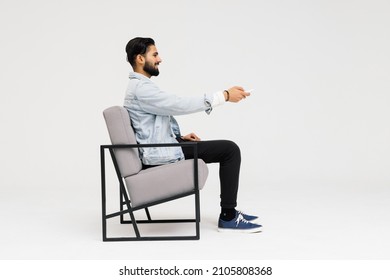 Side view of Asian man sitting in the armchair while watching TV in the studio