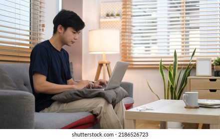 Side View Asian Man Sitting On Sofa And Using Laptop Computer.