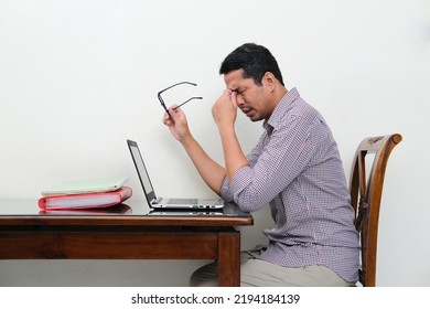 Side View Of Asian Man Sitting In Front Of Laptop Showing Tiredness