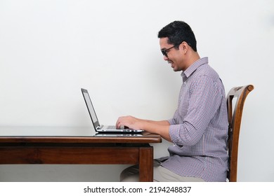 Side View Of Asian Man Typing On His Laptop With Happy Expression