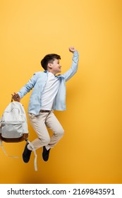 Side View Of Asian Schoolboy Holding Backpack And Jumping Isolated On Yellow