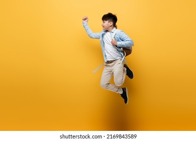 Side View Of Asian Schoolkid With Backpack Jumping On Yellow Background