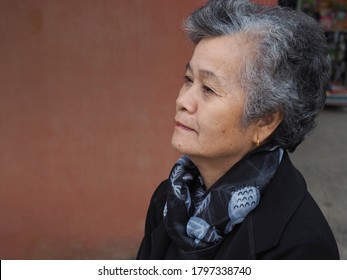 Side View Of An Asian Senior Woman Smiling And Looking Away While Sitting On Chair. Space For Text. Concept Of Old People And Healthcare