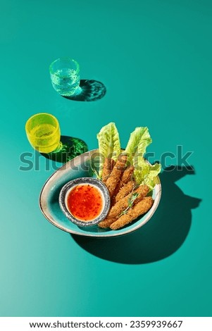 Side view of an Asian snack - Chicken tempura with sweet chili sauce. Green monochrome background, colored glasses. Minimalistic restaurant menu photo. Bright light, hard shadows.