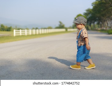 Side View Of Asian Toddler Boy In Bib Jeans Walking Cross The Road Lonely Copy Space. Infant Concept.