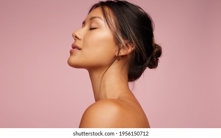 Side view of asian woman with beautiful skin. Female model with flawless skin on pink background.