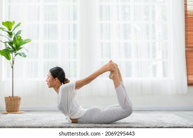 Side view of Asian woman doing Yoga exercise.Yoga bow or dhanurasana pose.Calm of healthy young female breathing and meditation with yoga at home. Exercise self care for wellness life - Powered by Shutterstock