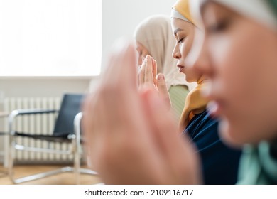 Side view of asian woman praying near blurred family at home