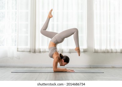 Side view of Asian woman wearing green sportwear doing Yoga Balance exercise in front of windows,Yoga HandStand pose or Pincha Mayurasana,Calm of healthy woman breathing and meditation yoga at home