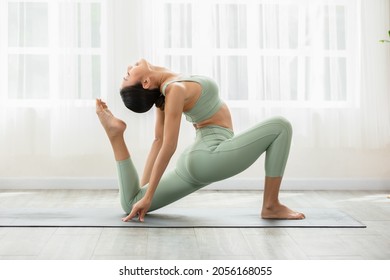 Vista lateral de una mujer asiática con ropa deportiva verde haciendo ejercicio de Yoga, pose de paloma real de una leyenda de yoga o de Eka Pada Rajakapotasana, calma de una joven saludable respiración y meditación con yoga en casa