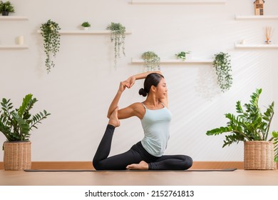 Side View Asian Woman Wearing Green Sportwear Doing Yoga Exercise.Yoga One Legged King Pigeon Pose Or Eka Pada Rajakapotasana.Calm Of Healthy Young Female Breathing And Meditation Yoga At Cozy Home