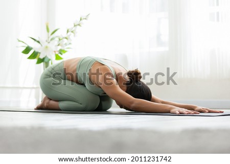 Side view of Asian woman wearing green sportwear doing Yoga exercise,Yoga Child’s pose or Balasana,Calm of healthy young woman breathing and meditation with yoga at home,Exercise for wellness life
