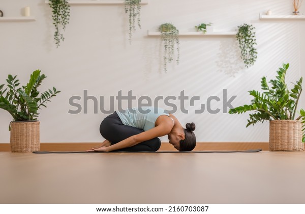 Side view of Asian woman wearing green sportwear\
doing Yoga exercise,Yoga Child’s pose or Balasana,Calm of healthy\
young woman breathing meditation with yoga at home,Exercise for\
wellness life