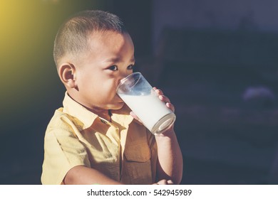 Side View Of Asian Young Boy Drinking Milk. On Dark Background