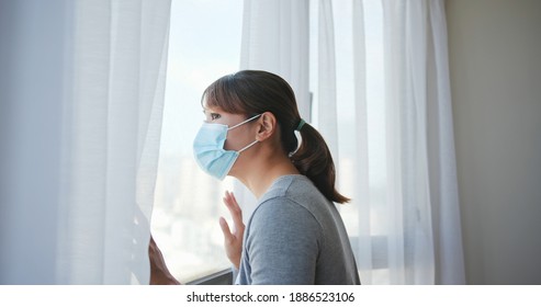 Side View Asian Young Woman Wearing Face Mask Stay Isolation At Home For Self Quarantine Due To Epidemic Of COVID19 - She Looks Out The Window