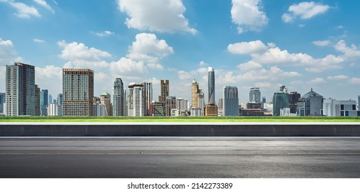 Side view of asphalt road highway with green grass and modern city skyline in background. - Shutterstock ID 2142273389