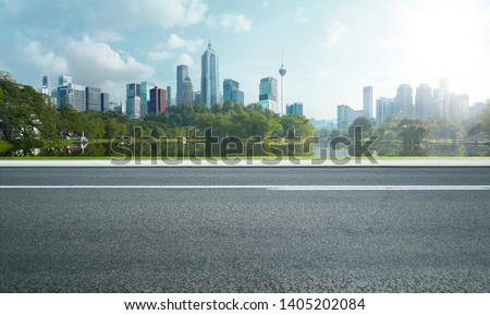 Side view of asphalt road highway with lake garden and modern city skyline in background.