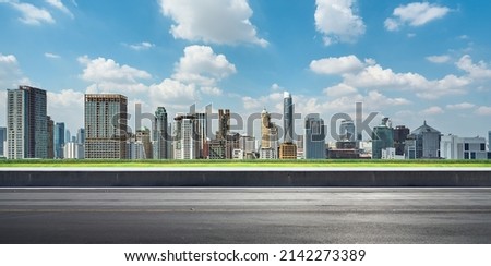 Side view of asphalt road highway with green grass and modern city skyline in background.
