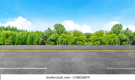 Side View Of Asphalt Straight Street Roadway Of Lanes With Lines And Green Trees With Blue Sky In Background.