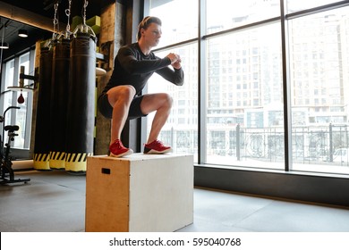 Side view of Athletic man which jumping on box in gym with window on background