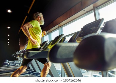 Side View Of A Athletic Middle Aged Man In Sportswear Running On A Treadmill In A Gym, Doing Cardio Before Workout