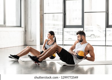 side view of athletic young couple in sportswear holding medicine balls and exercising on yoga mats in gym - Powered by Shutterstock