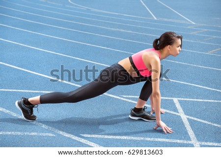 Side view of athletic young woman in sportswear on starting line ready to run 