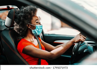 Side view of attractive african woman with short curly hair with face mask on sitting and driving car. Prevention from spreading corona virus / covid 19 concept.