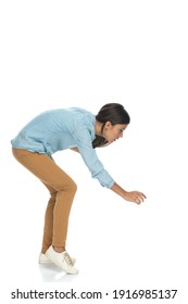 side view of an attractive casual woman bending down and trying to grab something against white background