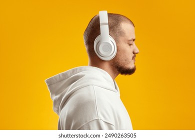 Side view of attractive caucasian guy wearing white hoodie and headphones, listening music with closed eyes, isolated over yellow background - Powered by Shutterstock