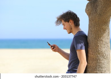 Side View Of An Attractive Man Using A Smart Phone On The Beach With The Sea And Horizon In The Background            