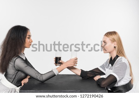 side view of attractive multiethnic women in black and white clothes holding glasses with milk and soda isolated on white
