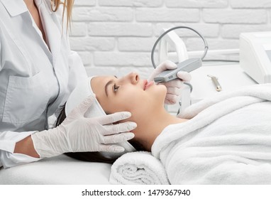 Side view of attractive woman lying on coach in beauty salon. Professional female doctor doing cleaning procedure of skin with scrubber in spa. Concept of cosmetology and dermatology.