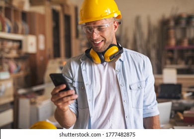 Side view of an attractive young joiner at his workplace, holding his smartphone and having a good laugh.  - Powered by Shutterstock